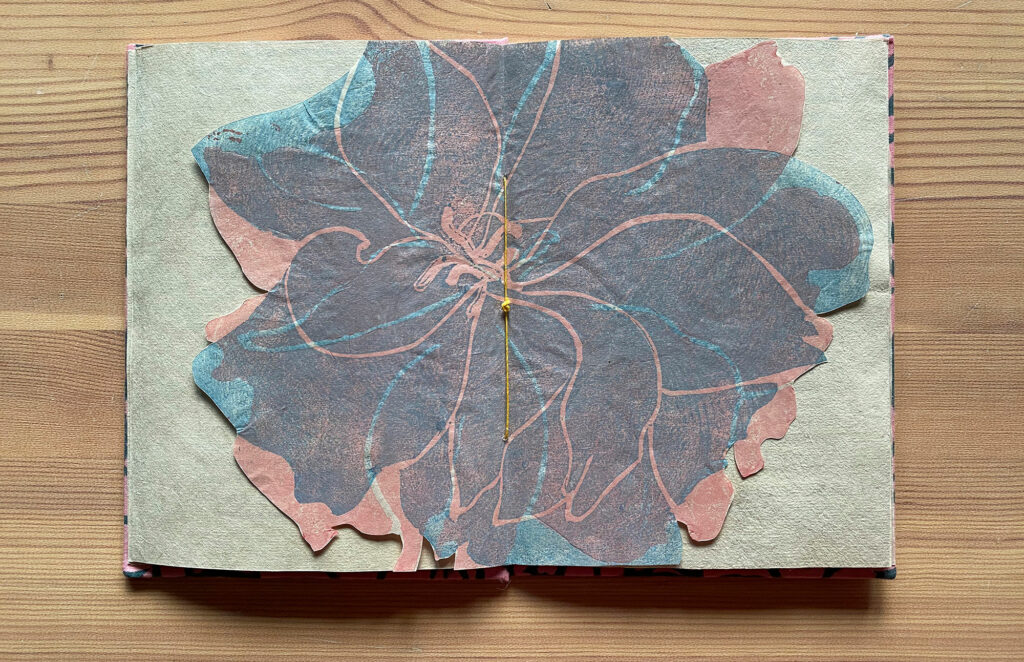 open book showing center spread of a cutout of a blue and pink cherry blossom flower, Untitled artist’s book, 2020, Artist’s book, single section case binding structure, pages are made with archival Okawara paper, woodcut prints on endsheets and spread on Kitakata paper